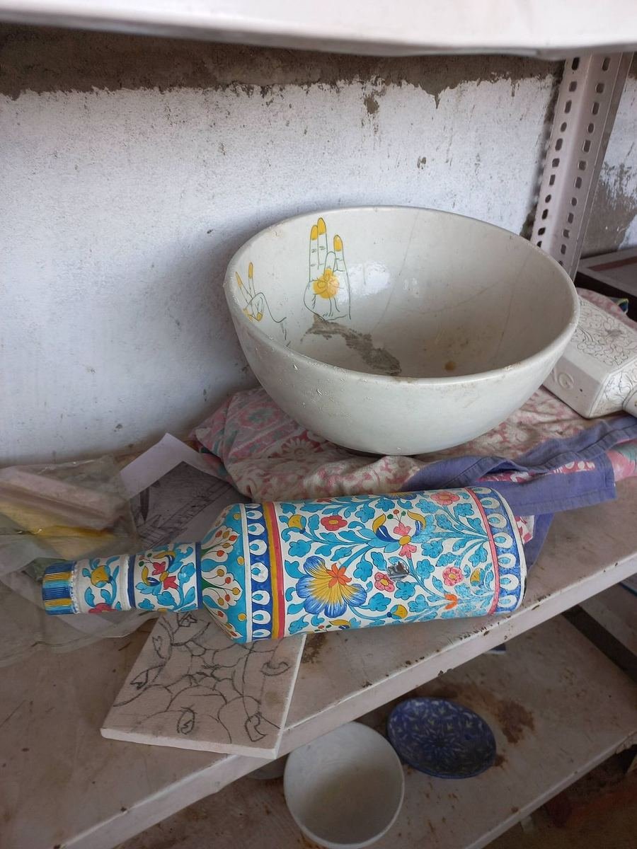 Eine Vase aus blauer Keramik wird in einer Werkstatt in Multan bemalt, daneben wartet eine vorgezeichnete Schale auf Farbe